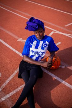 Stylish woman in blue jersey holding a basketball on a sports track.