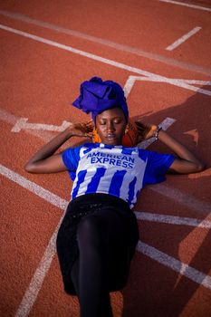 Woman in vibrant attire relaxes on a sports track, cradling a basketball.