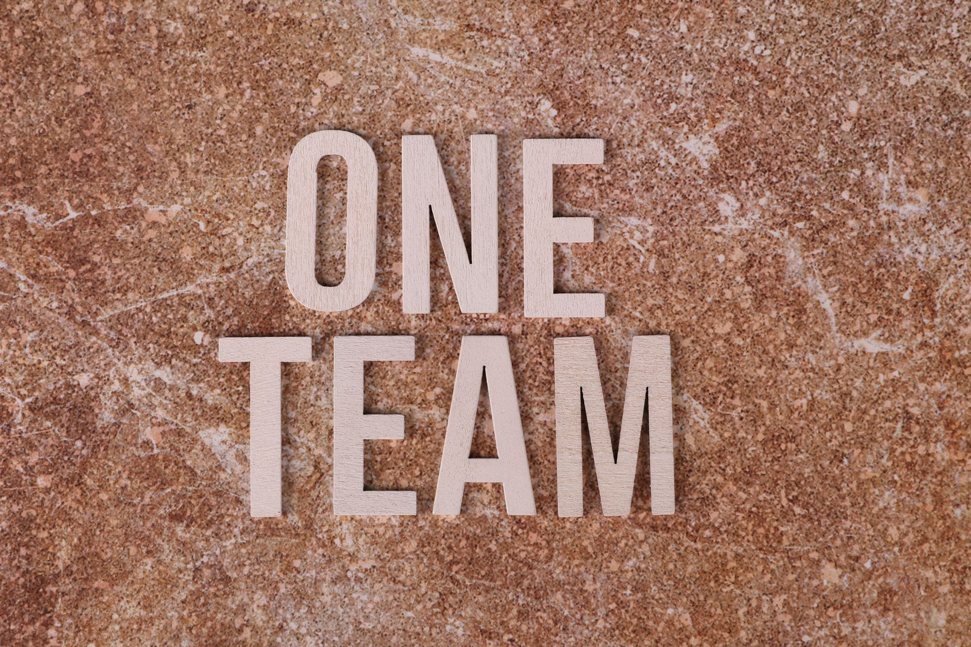 Wooden 'One Team' text on marble background symbolizing unity and teamwork.