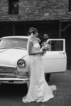 A bride and groom posing with a classic vintage car on their wedding day.