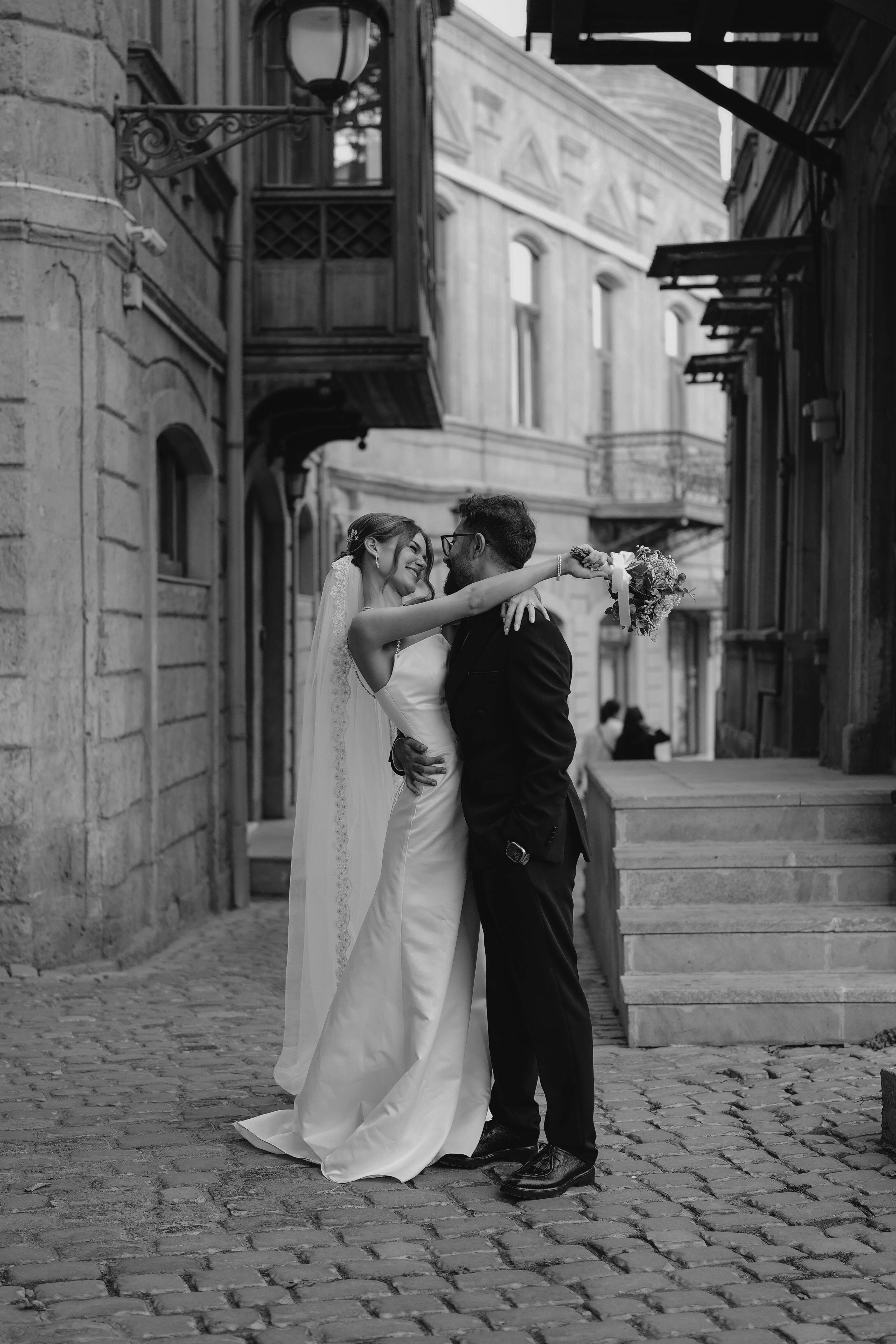 Elegant black and white photo of a couple embracing in a historic alleyway setting.