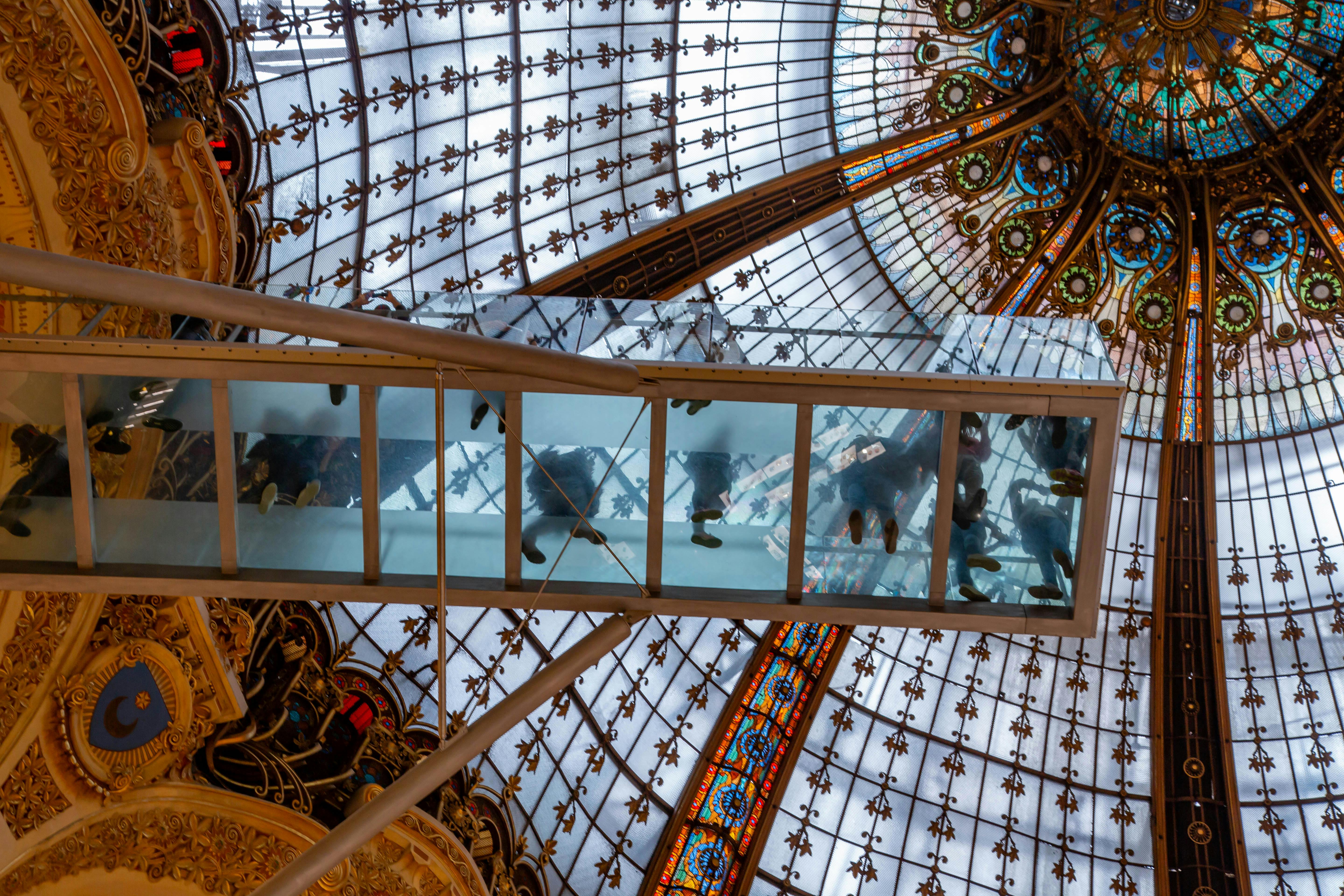 Intricate stained glass dome with people walking above at Galeries Lafayette, Paris.