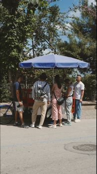 A group of adults enjoying a sunny day at an outdoor ice cream stand.
