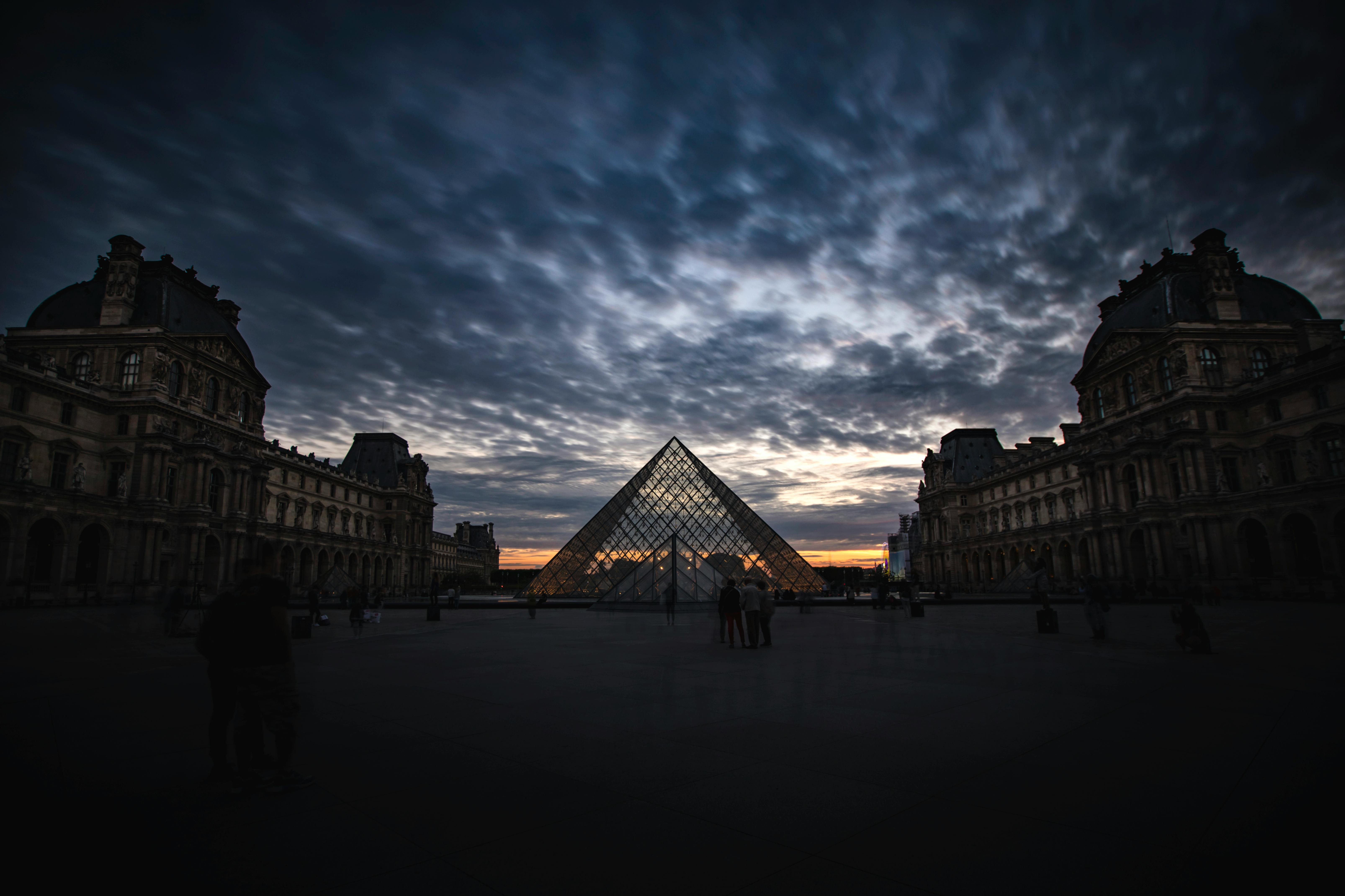 Silhouette of the Louvre Pyramid at sunset with dramatic clouds in Paris.