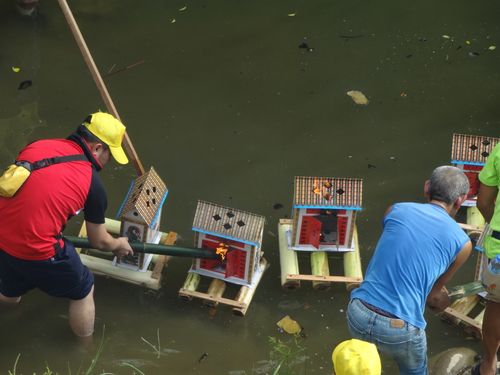 Free Three men set fire to miniature houses floating on a river in a ceremonial activity. Stock Photo