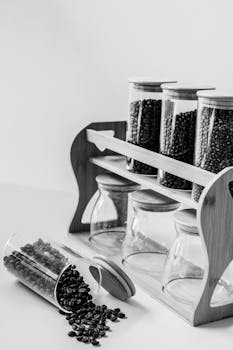 Black and white image of glass jars with coffee beans on a wooden rack.