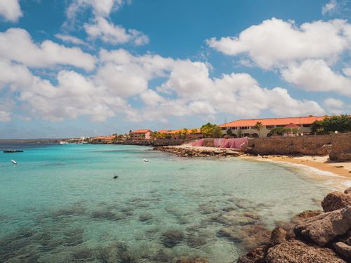 Free Beautiful seaside view with turquoise waters, sandy beach, and colorful buildings under a bright blue sky. Stock Photo