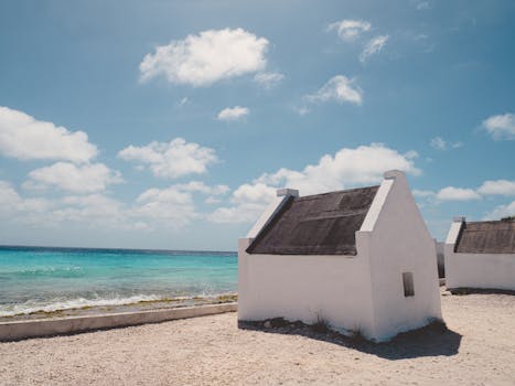 Whitewashed slave huts by the clear blue Caribbean sea under a vibrant sky.
