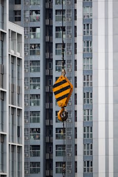 Close-up of a tower crane hook against high-rise buildings, symbolizing urban development.