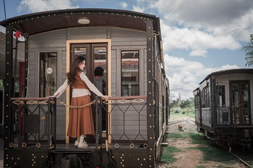 Free Elegant woman standing on an ornate vintage train car outdoors, under a bright sky. Stock Photo