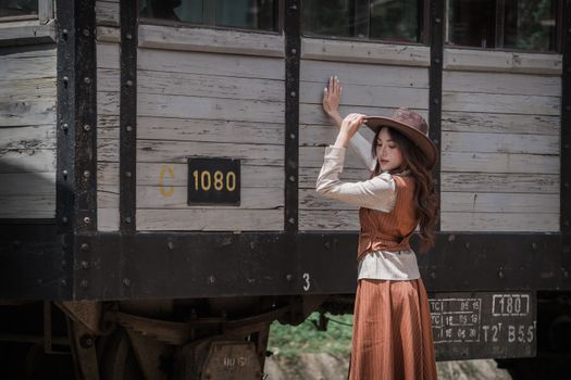 A woman in a vintage outfit standing next to a historical train carriage outdoors.