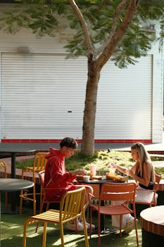 A young couple enjoys a sunny outdoor picnic with burgers, seated across from each other at a table.