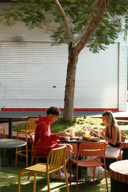 A young couple enjoys a sunny outdoor picnic with burgers, seated across from each other at a table.