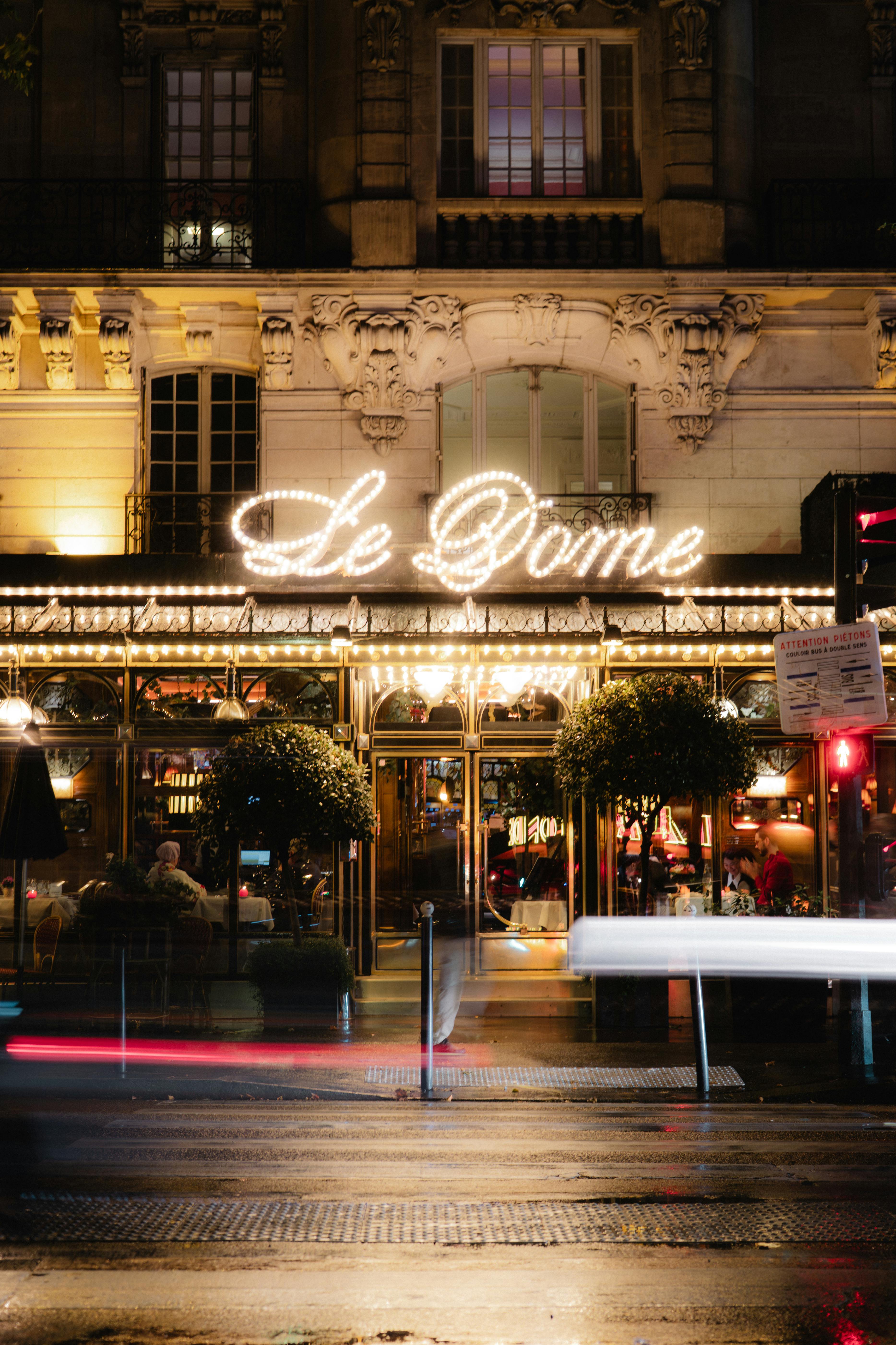 Vibrant nighttime view of Le Dôme Café in Paris with neon lights and lively street scene.