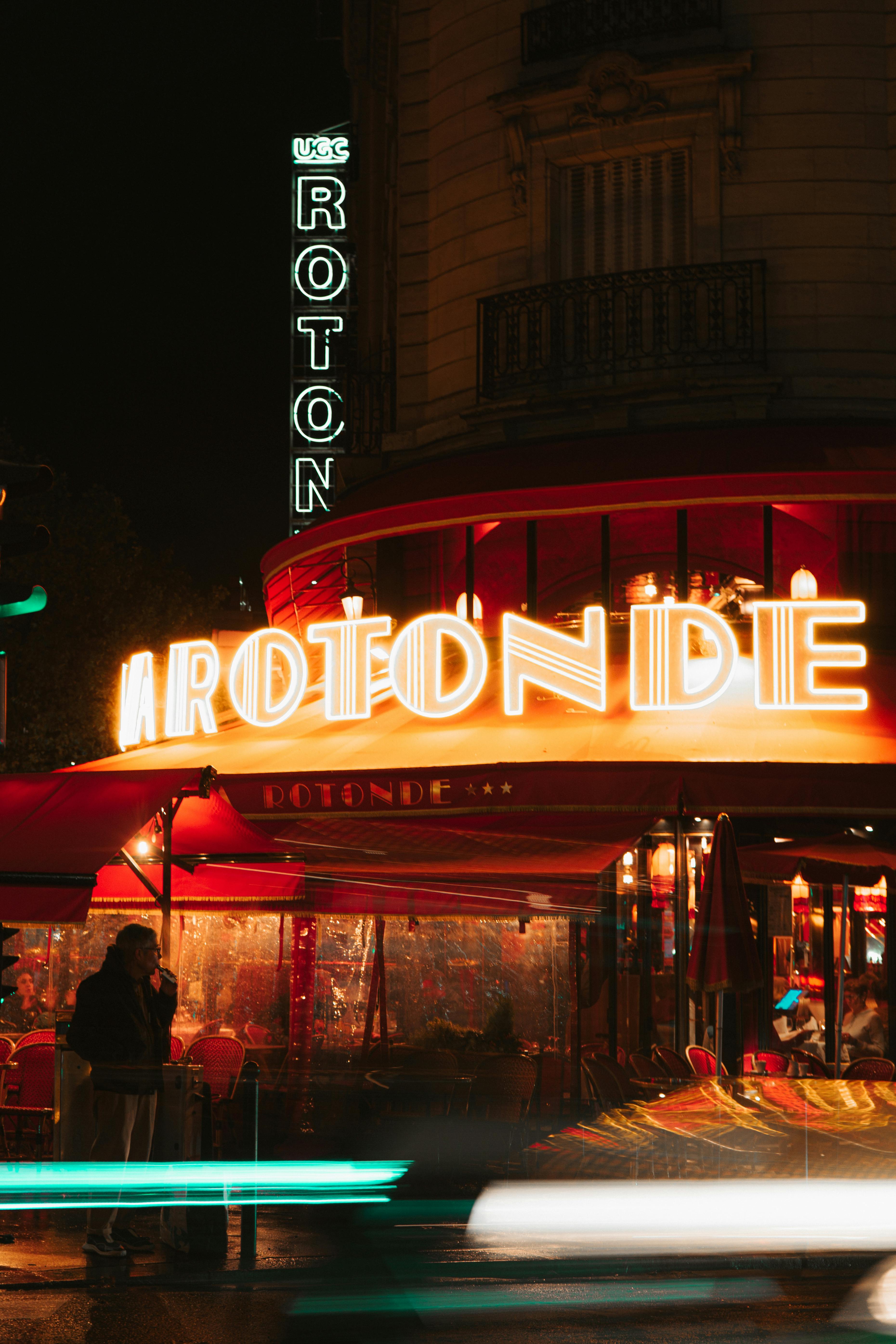 A vibrant night scene at La Rotonde cafe in Paris with neon lights.