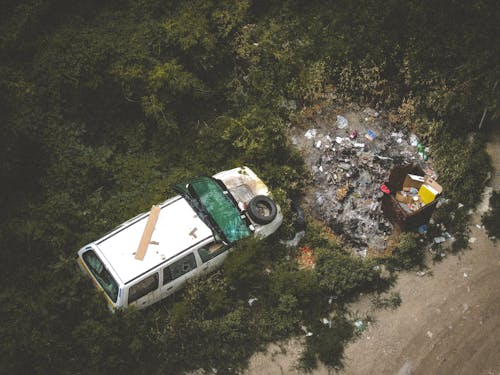 ゴミ箱の近くの白い損傷した車両の鳥瞰図写真