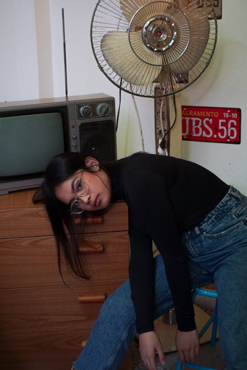 Женщина наклоняется перед выключенным телевизором и вентилятором