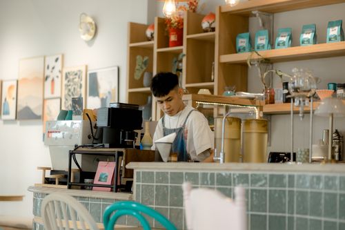 Free A barista making coffee in a cozy café, surrounded by modern interior design and warm ambiance. Stock Photo