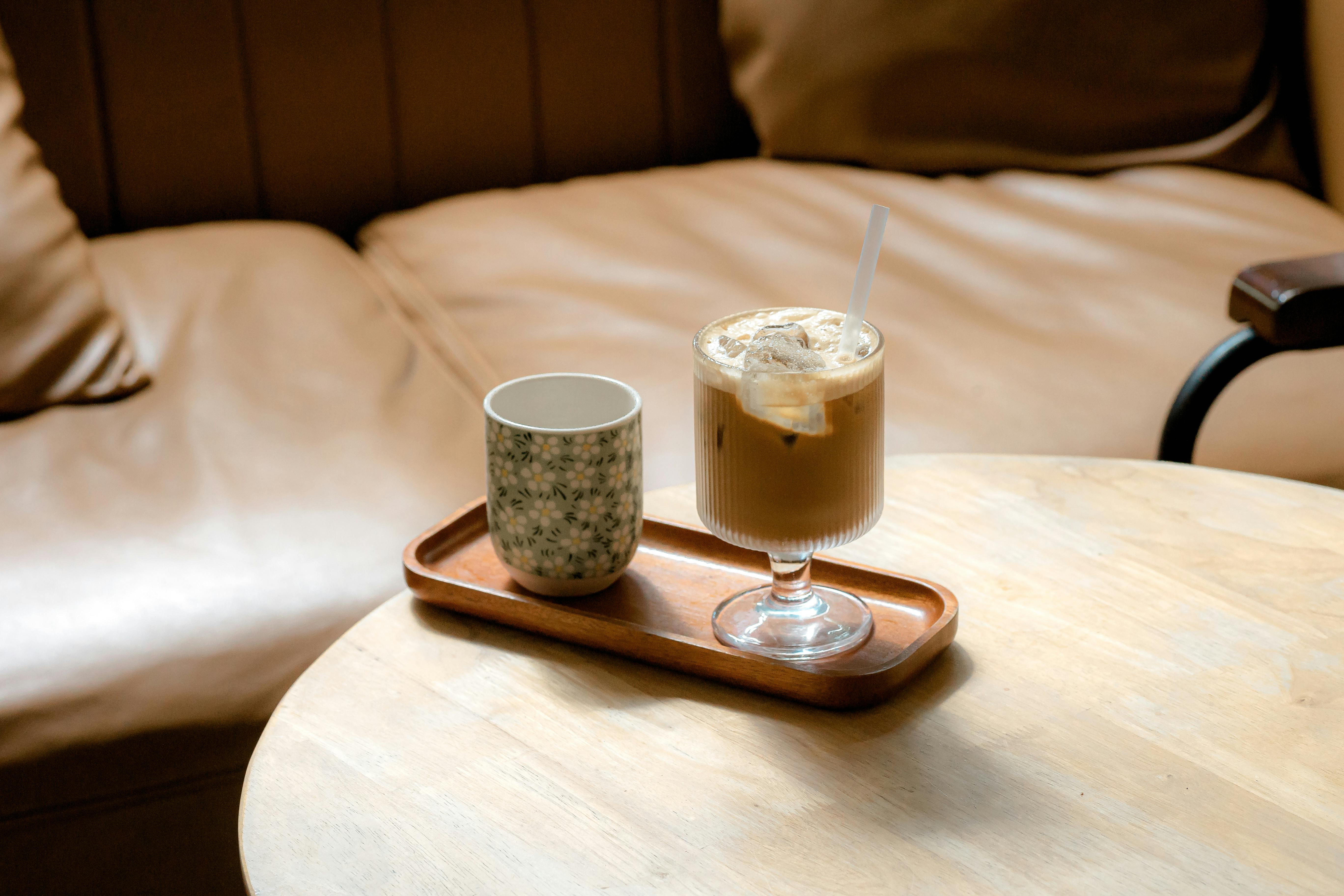 Warm, inviting coffee lounge scene featuring an iced latte and a ceramic mug on a wooden table.
