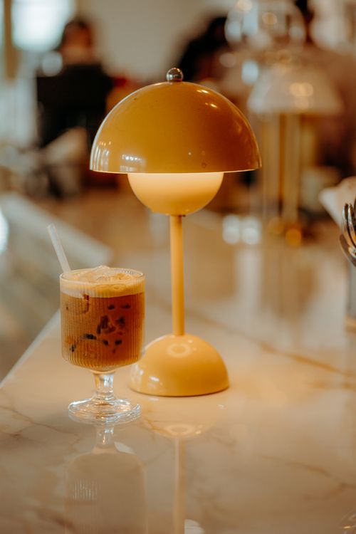 Free Stylish coffee shop scene featuring iced coffee and modern lamp on marble counter. Stock Photo