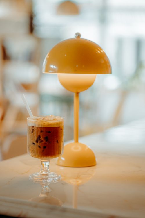 Free Warm cafe environment featuring an iced coffee and a stylish lamp on a marble table. Stock Photo