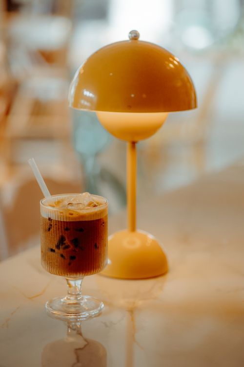 Free Warm café ambiance with a stylish lamp and iced coffee on a marble table. Stock Photo