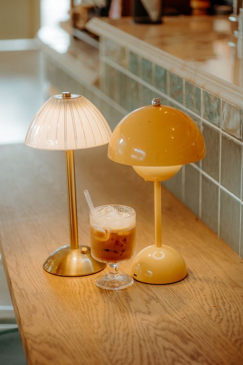 Free Warm café setting featuring two lamps and an iced coffee on a wooden counter. Stock Photo