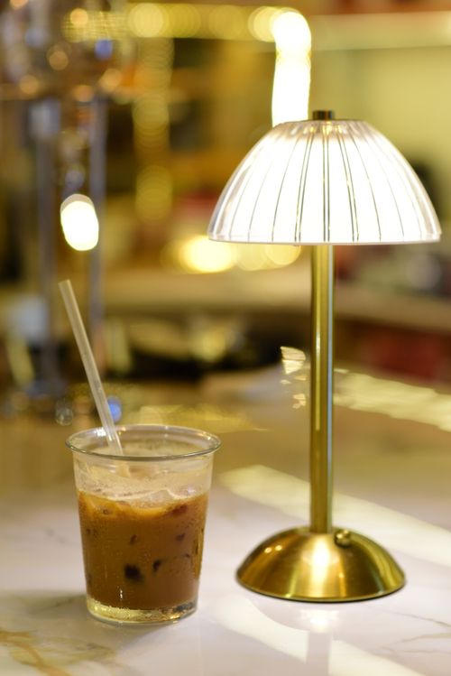 Free A warm, intimate cafe scene featuring an iced coffee and a glowing lamp on a marble table. Stock Photo