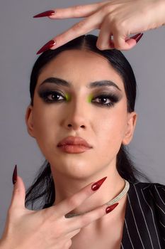 Close-up portrait of a stylish woman with bold makeup and striking red nails, exuding confidence.