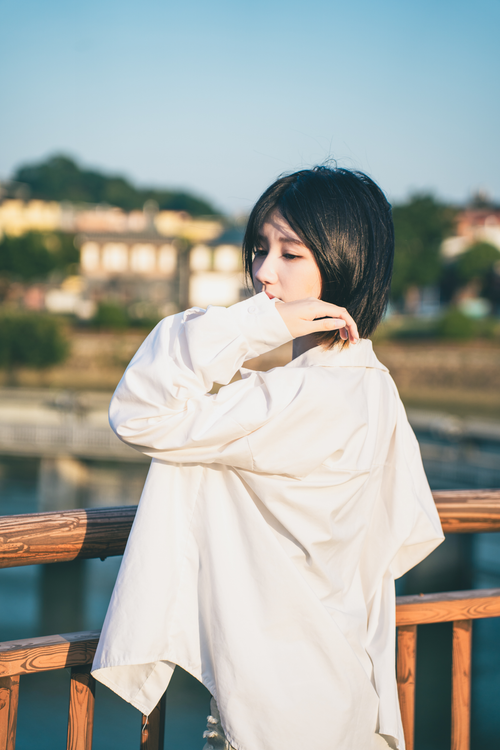 Free Woman in a white shirt pensively enjoying a sunny day outdoors against a blurred background. Stock Photo
