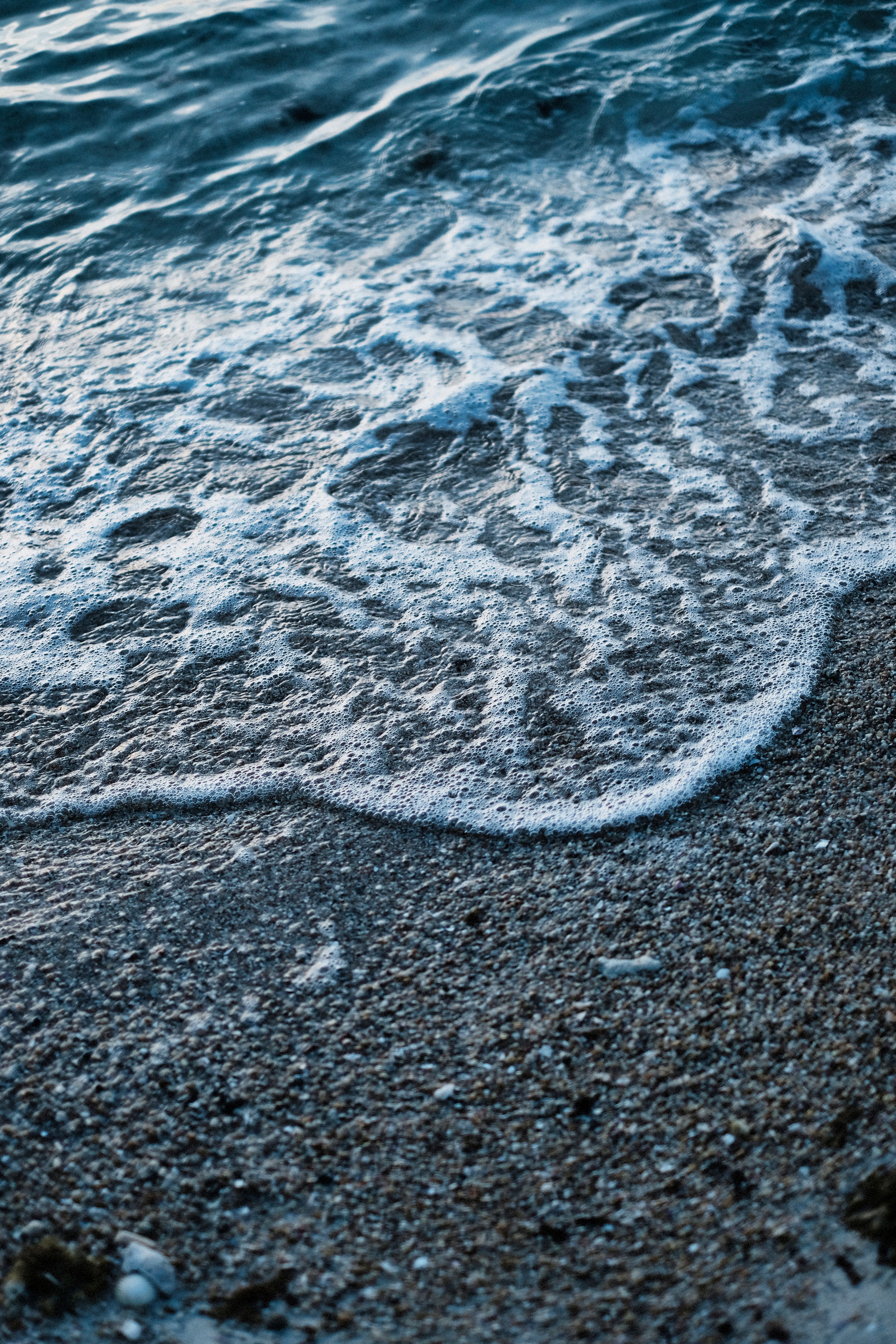 Soft waves roll onto a pebble beach during twilight, creating a serene coastal scene.
