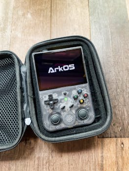 Close-up of a gaming console displaying ArkOS, showcasing buttons and controls in a hard case.