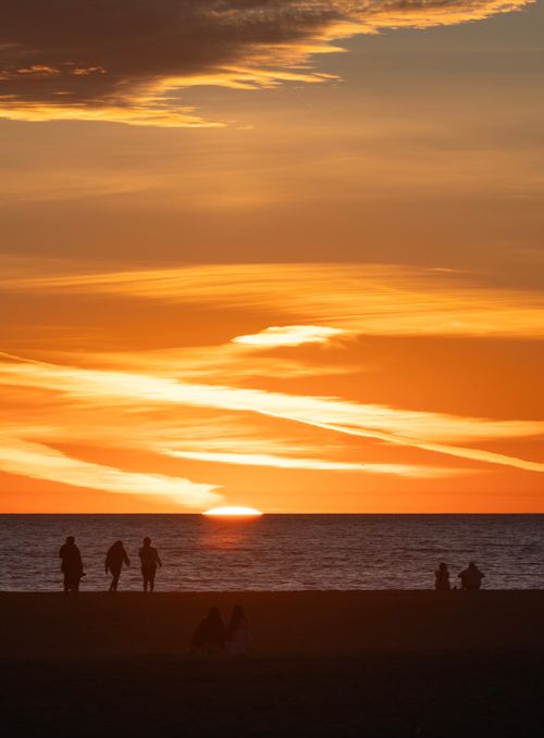 Free Silhouetted people by the beach enjoying a vibrant orange sunset over the ocean. Stock Photo