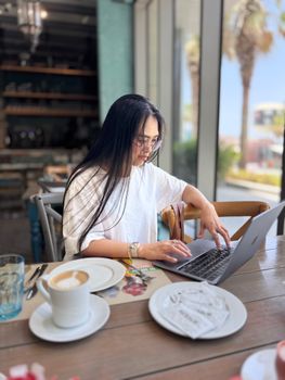 Focused woman typing on laptop in stylish cafe with coffee and pastries.