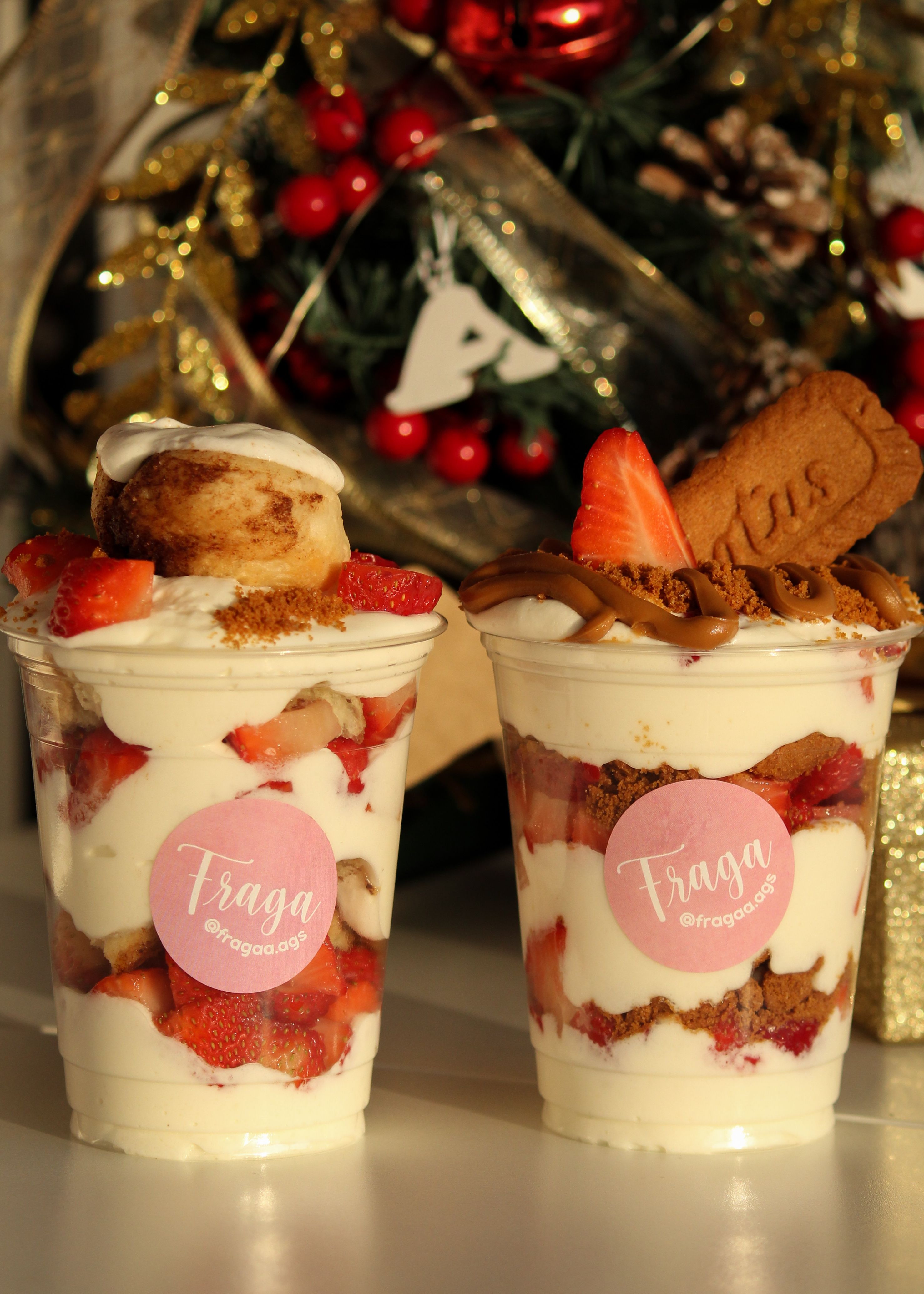 Two strawberry parfait cups with biscuits in front of Christmas decorations, perfect for festive gatherings.