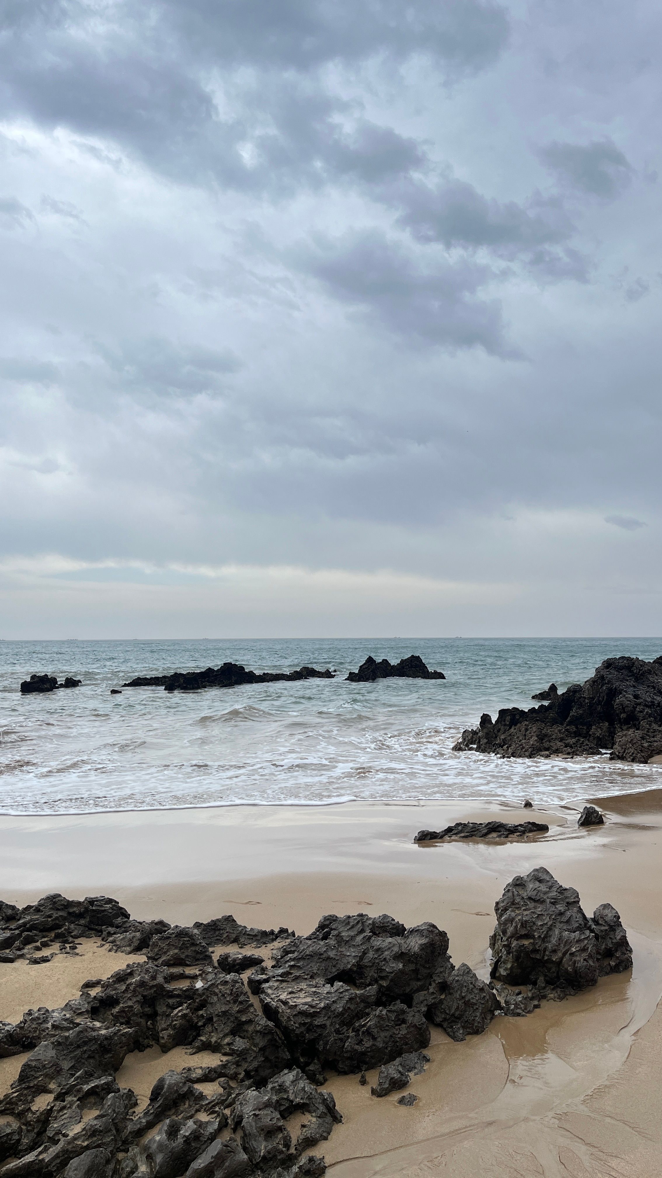 A beach with wet sand and calm waves under a cloudy sky after rain