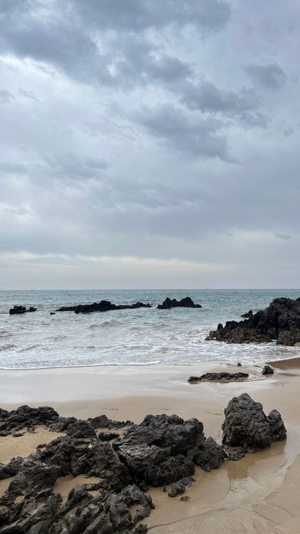 A beach with wet sand and calm waves under a cloudy sky after rain