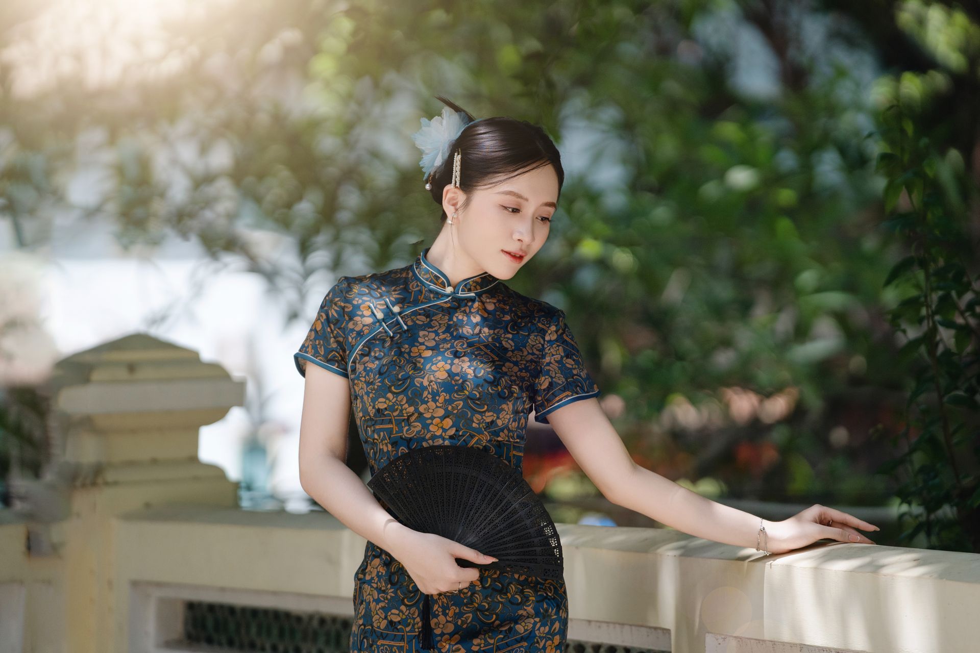 Elegant woman in traditional dress holding fan in serene outdoor setting, exuding grace.