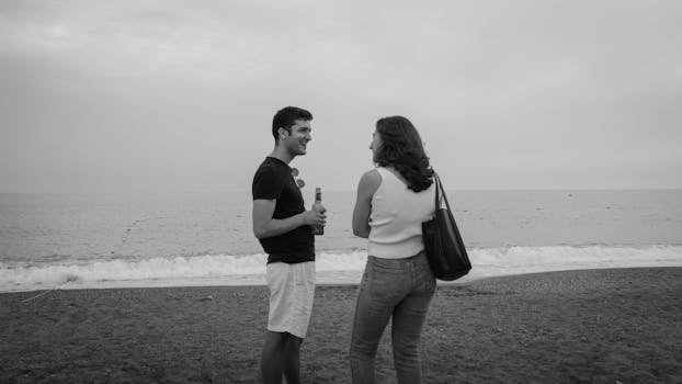 Black and white photo of two friends having a casual conversation on a beach.