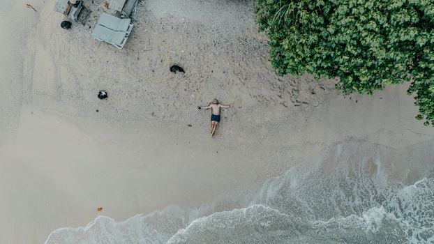Aerial shot of a serene beach in Sri Lanka with a lone person lying on the sand near lush greenery.