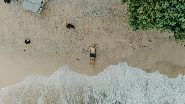 A tranquil aerial shot captures a person resting on a sandy beach by the ocean in Sri Lanka.