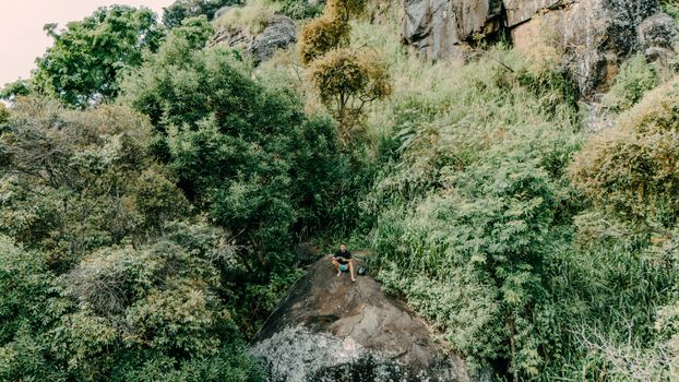 Aerial shot of a person perched on a rock amidst dense greenery in Sri Lanka's landscape.