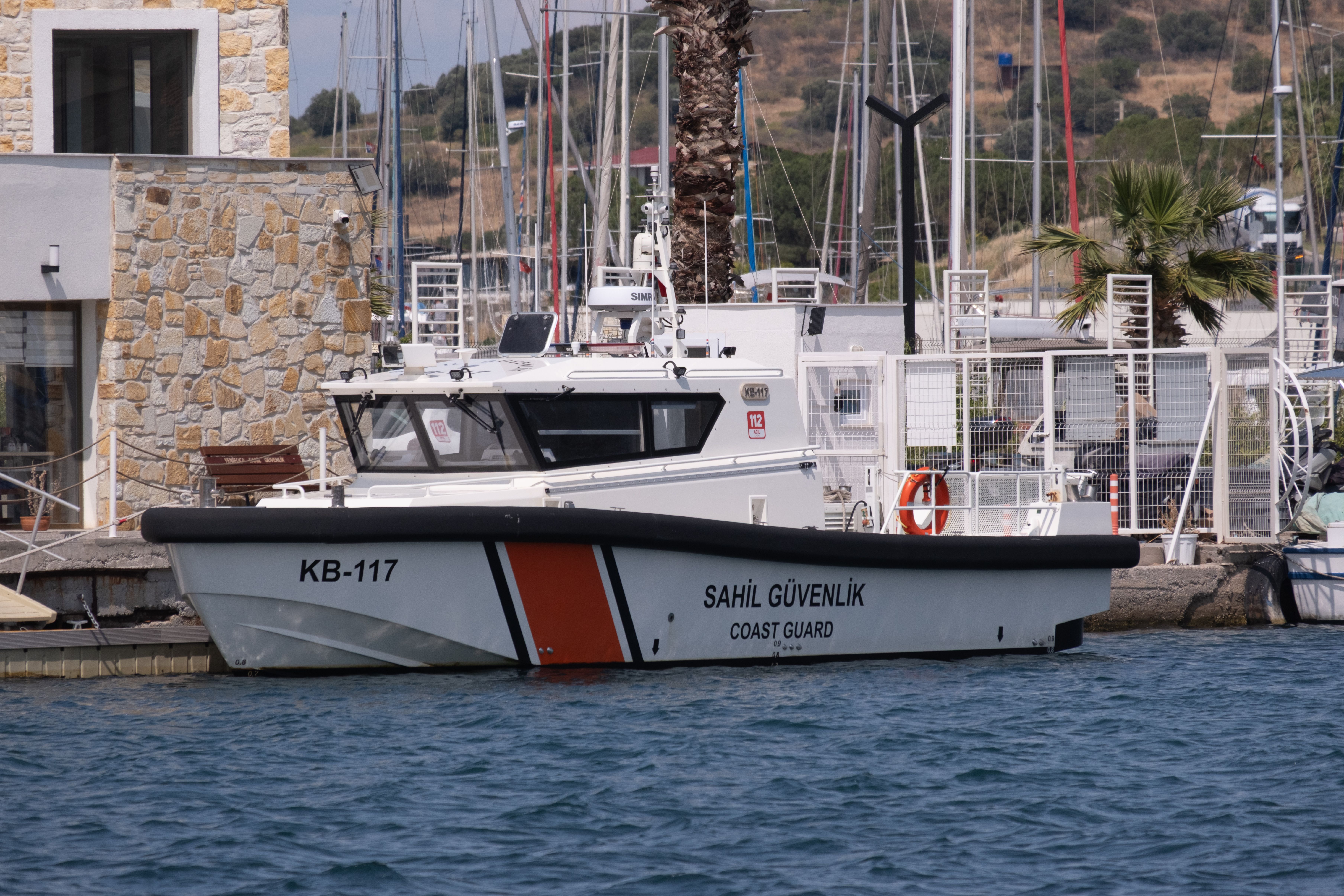 Coast Guard patrol boat moored at a marina, with yachts and waterfront buildings in the background