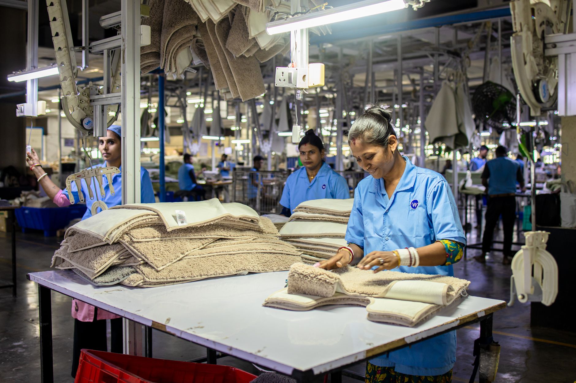 Factory workers sorting and folding fabric on a textile line, the kind of back-end labour most shoppers never see when a basics brand sells itself as pure and simple.