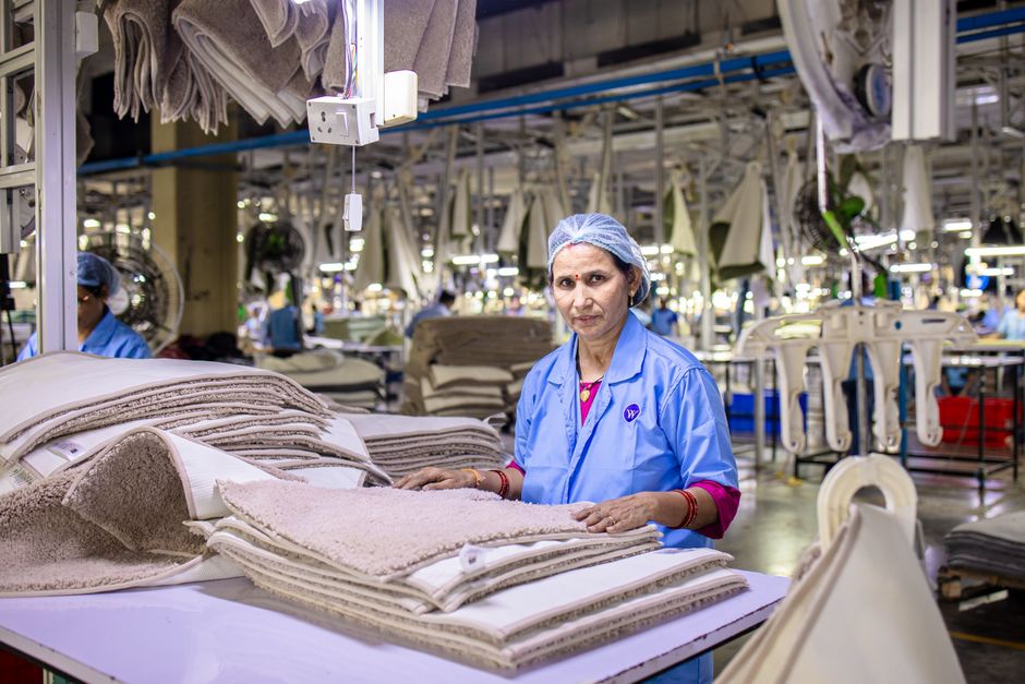Adult female worker in a textile factory sorting fabric materials under bright industrial lighting.