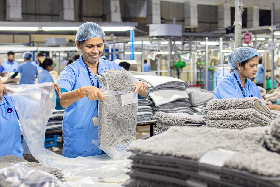 Indian factory workers sorting gray rugs in a textile manufacturing setting.