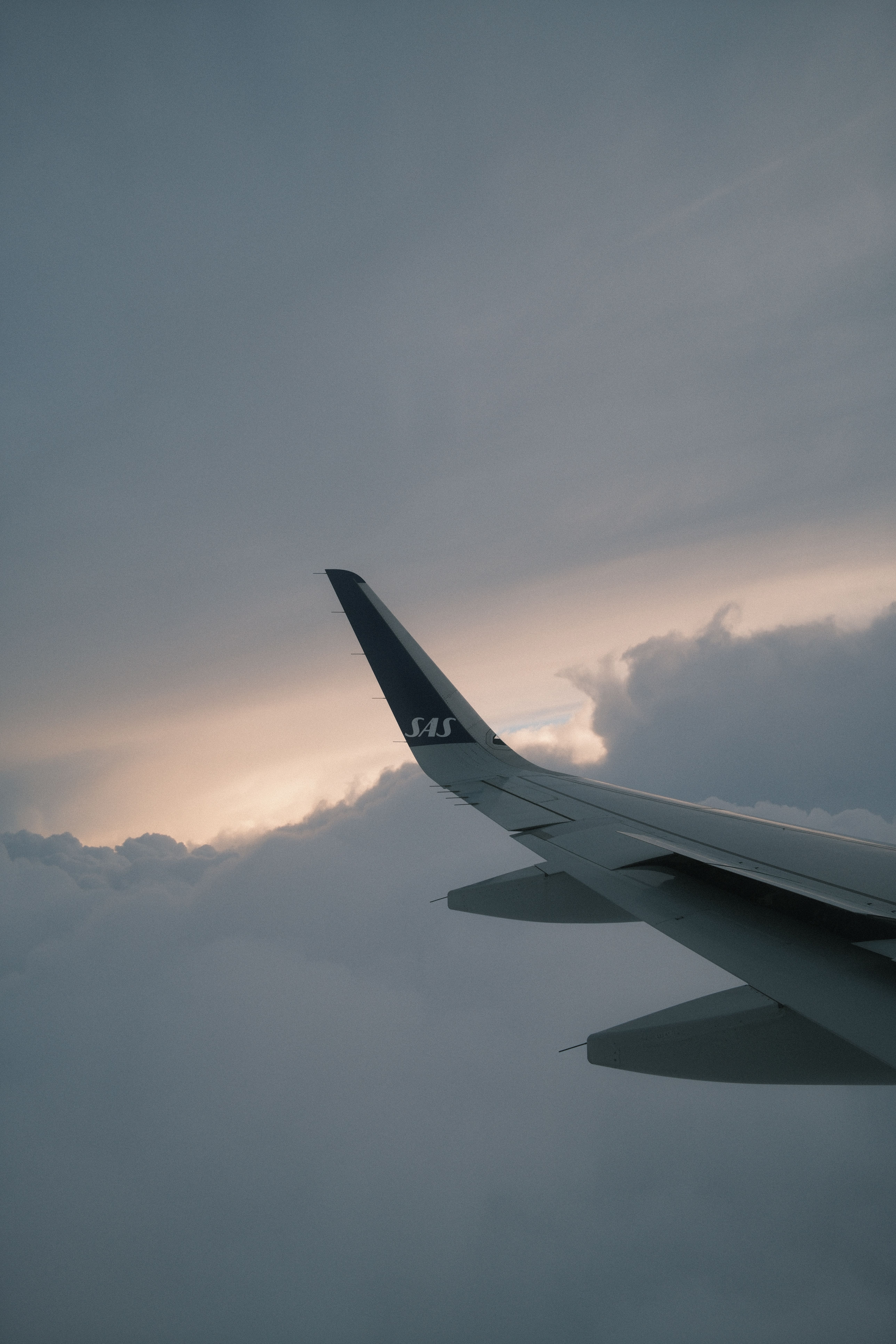 Dramatic view of an airplane wing during sunset above the clouds, capturing serene flight atmosphere.