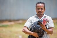 South Asian man smiling while holding a turkey on a sunny day in Chattogram, Bangladesh.