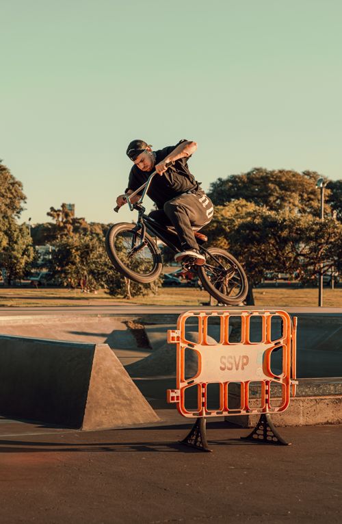 Free BMX rider executes a jump over a barrier in an outdoor skatepark during daylight. Stock Photo