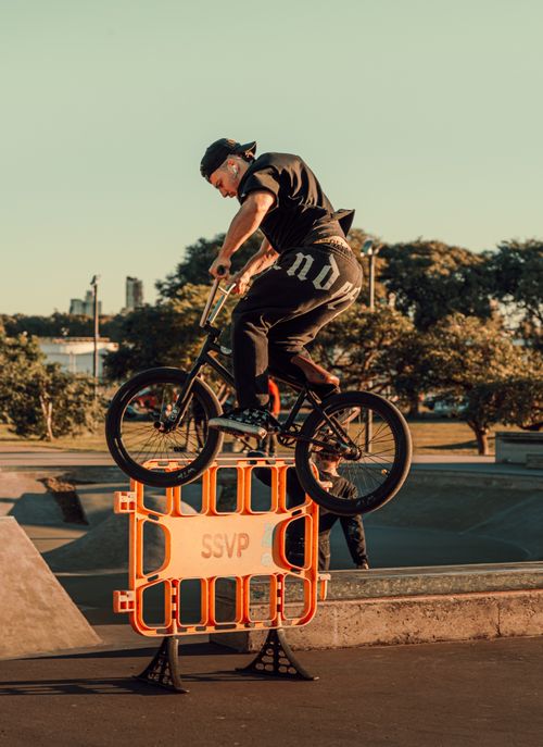 Free BMX rider performing a trick over an obstacle in a skatepark at sunset. Stock Photo
